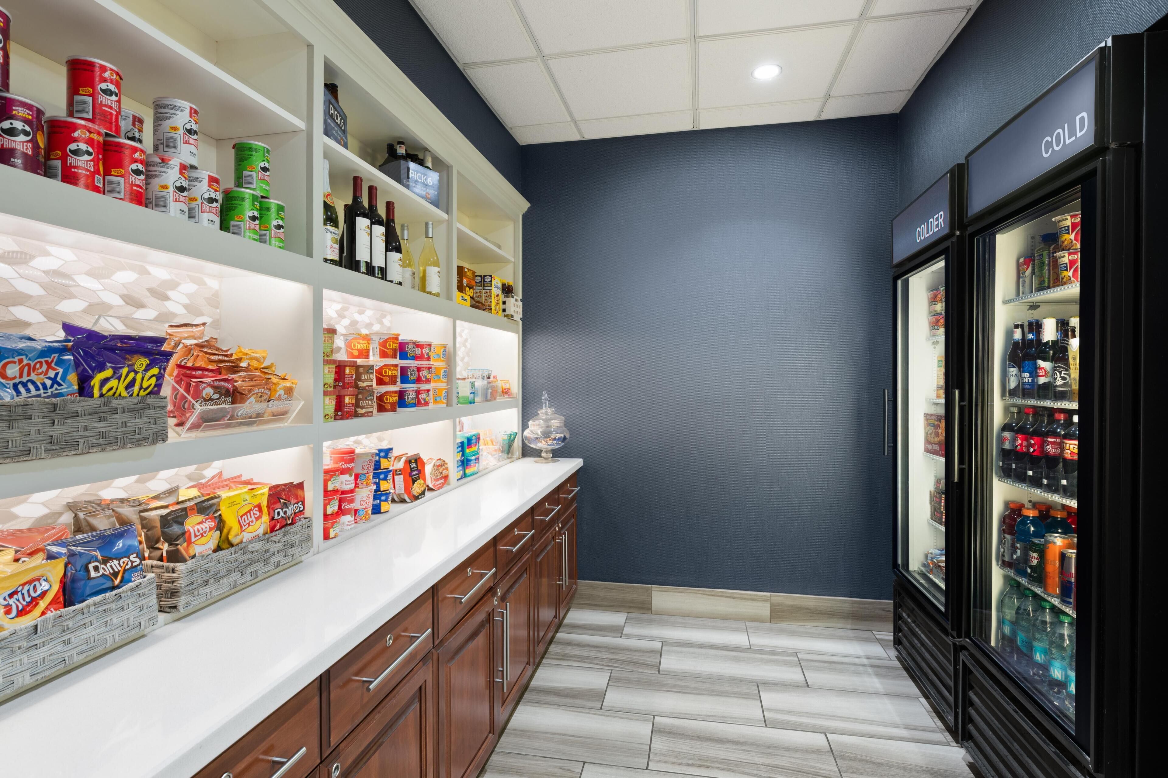 A kitchen with shelves stocked with snacks, a refrigerator, and a tiled floor.