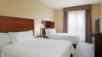 A hotel room with two beds, a nightstand with a lamp, a television, and a window with curtains.