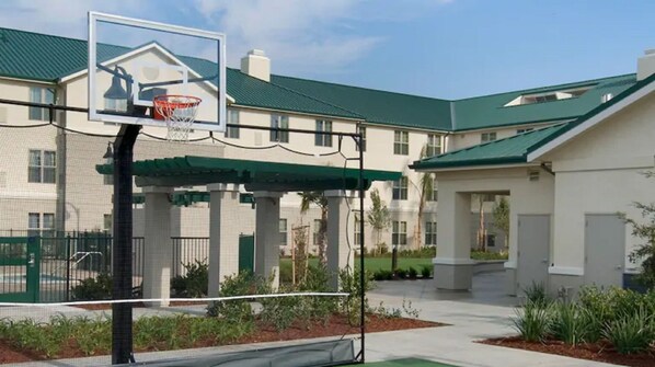 A basketball court with a hoop, surrounded by a covered seating area and a building with a green roof. - Homewood Suites By Hilton Sacramento Airport - Natomas (Sacramento)