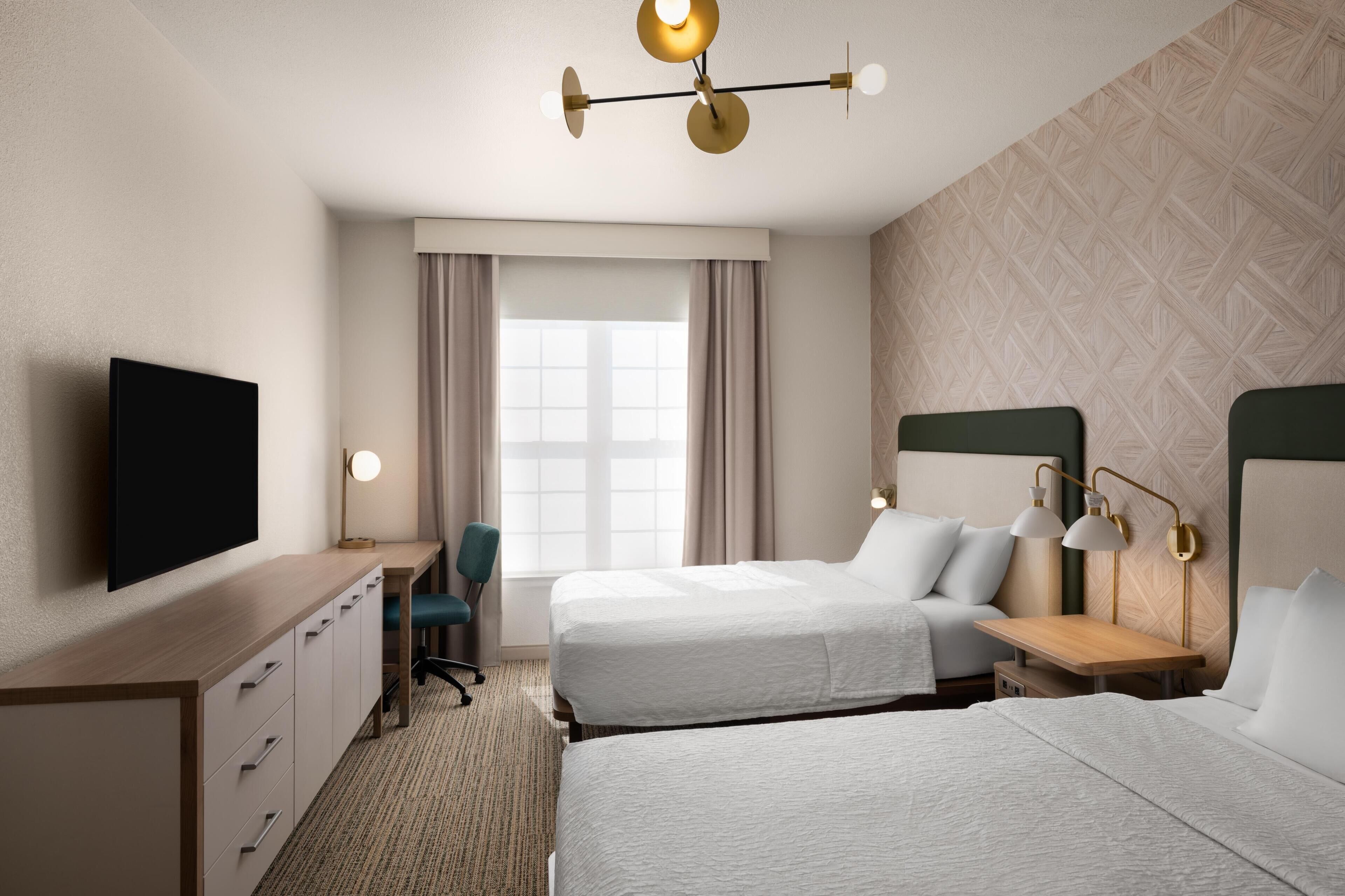 Een hotelkamer met twee bedden, een bureau, een stoel, een televisie en een raam met gordijnen.