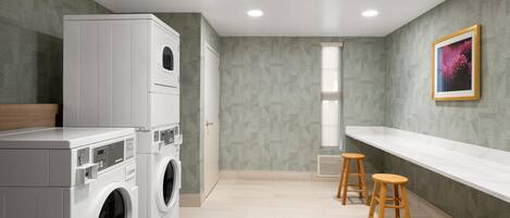 A laundry room with stacked washing machines, a drying rack, and wooden stools.