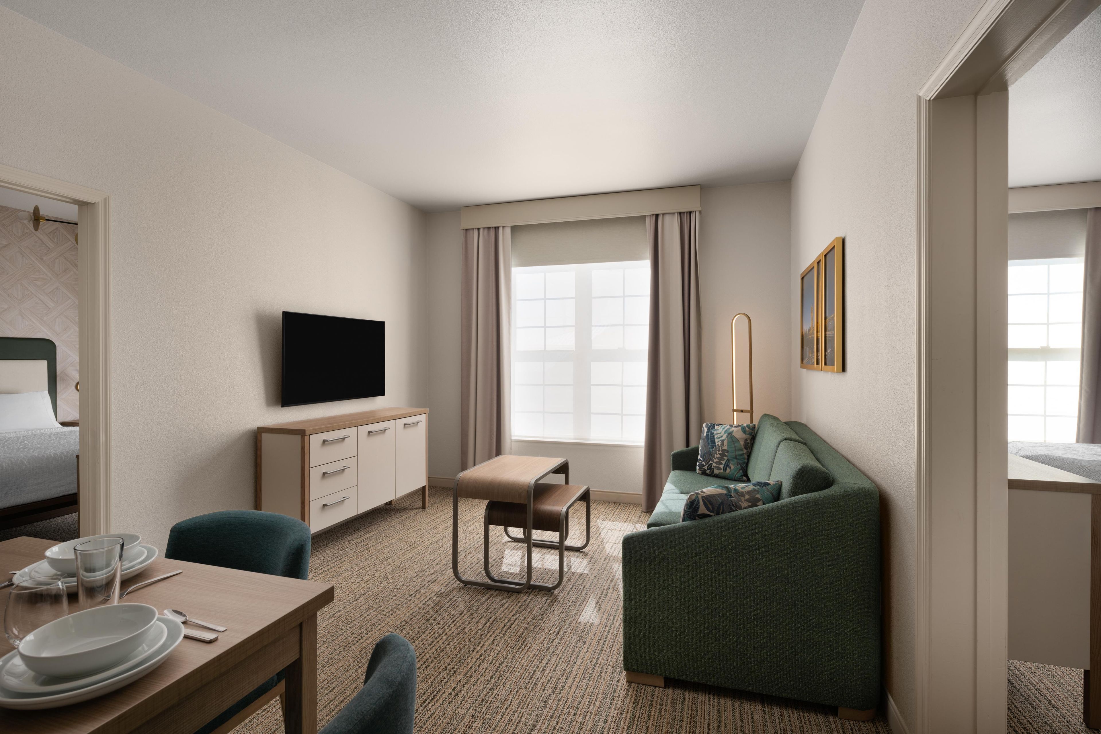 Een hotelkamer met een bed, een televisie, een bureau met een stoel, een bank en een raam met gordijnen.