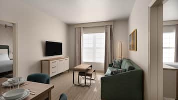 Una habitación de hotel con cama, televisión, escritorio con silla, sofá y ventana con cortinas.