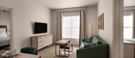 A hotel room with a bed, a TV, a desk with a chair, a sofa, and a window with curtains.