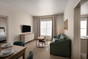 Ein Hotelzimmer mit einem Bett, einem Fernseher, einem Schreibtisch mit Stuhl, einer Couch und einem Fenster mit Vorhängen.