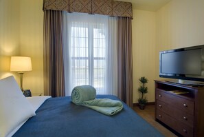A hotel room with a bed, a television on a wooden dresser, a lamp, and a window with curtains. - Homewood Suites By Hilton Sacramento Airport - Natomas (Sacramento)