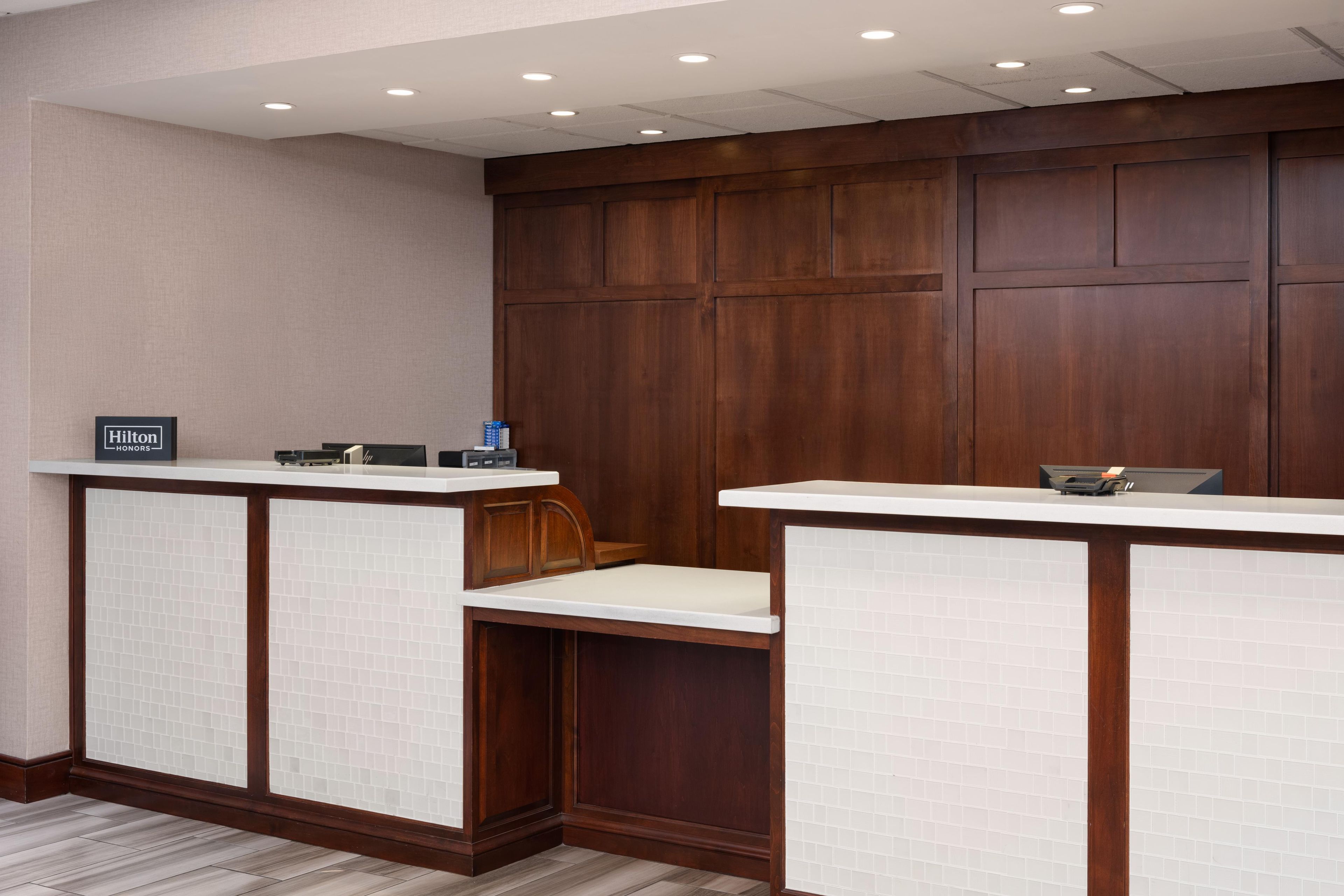 A hotel reception area with two counters, a wooden panel wall, and a tiled floor.