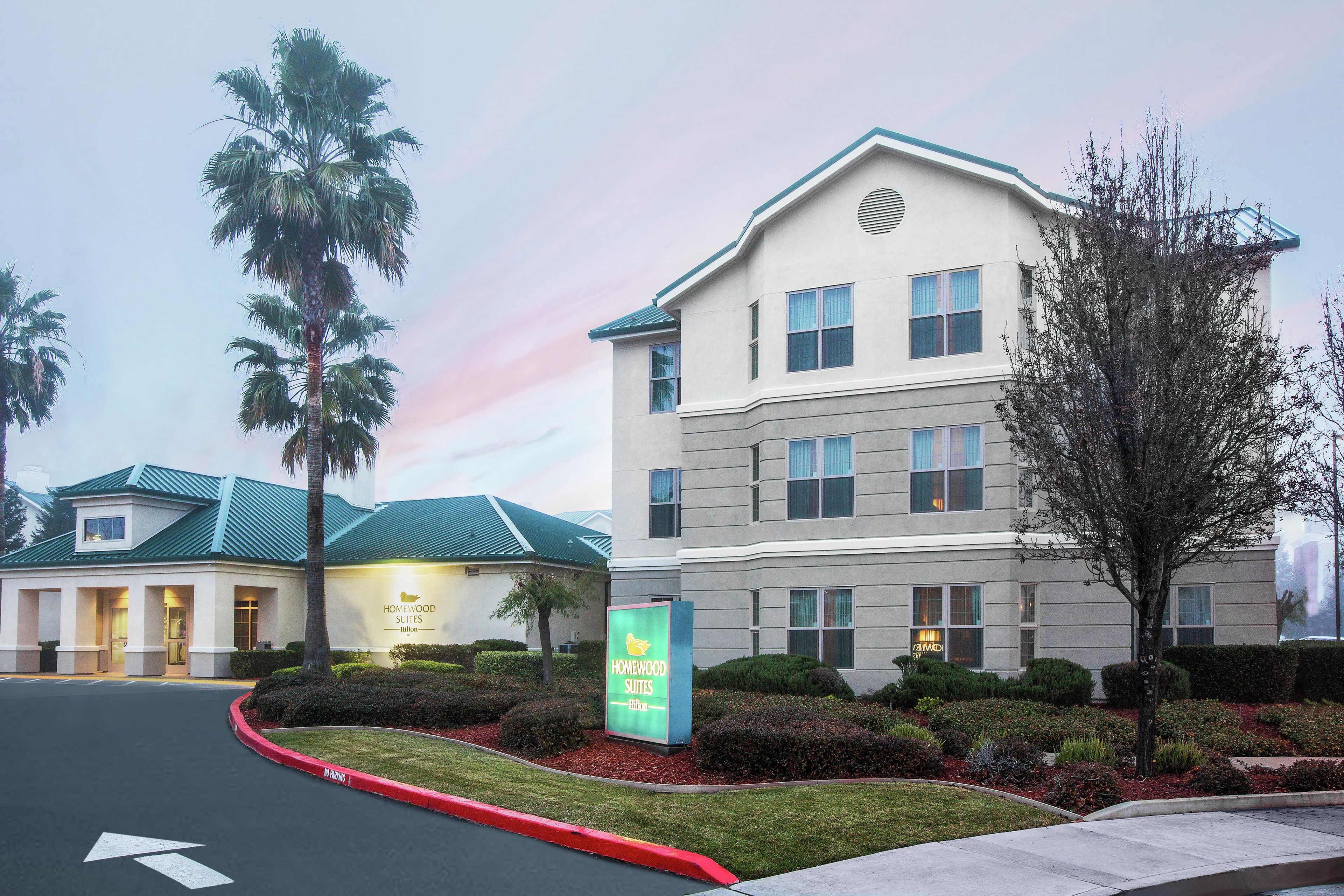 A hotel with a sign for Homewood Suites, a parking lot, and a building with a green roof.