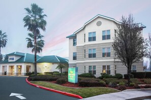 Un hotel con un letrero de Homewood Suites, un estacionamiento y un edificio con techo verde.