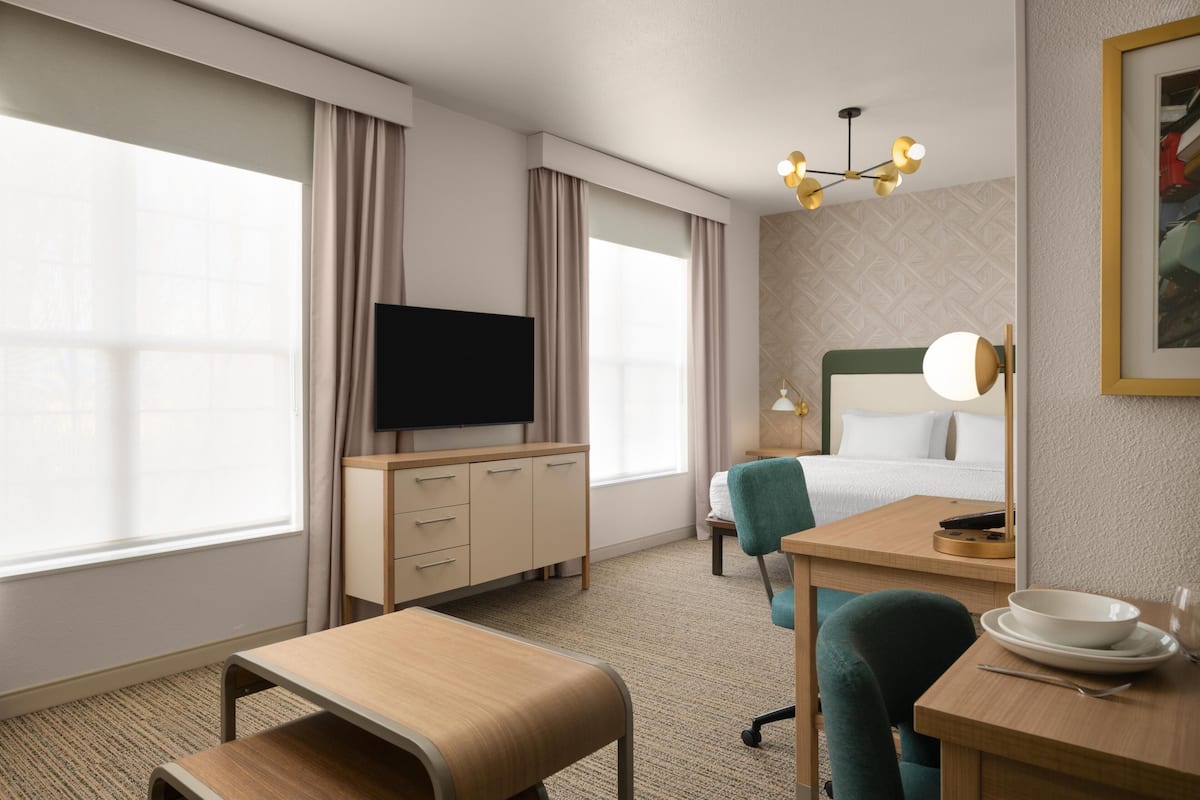 A hotel room with a bed, a desk with a chair, a television, and a dining table with a chair.