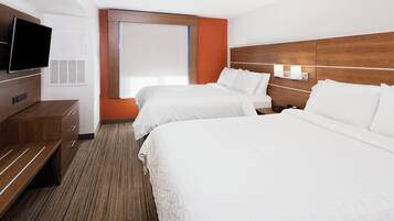 A hotel room with two beds, a TV, a desk, and a window with blinds.