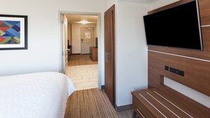 Een hotelkamer met een bed, een televisie bevestigd aan een houten paneel, en een gang naar een badkamer.