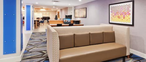 A hotel lobby with a seating area, a reception desk, and a dining area.