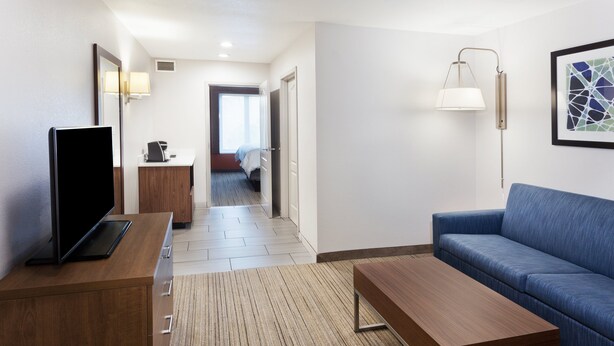 Een hotelkamer met een houten bureau, een blauwe bank, een flatscreen televisie, een nachtkastje, een lamp en een lijst met een kunstwerk aan de muur.