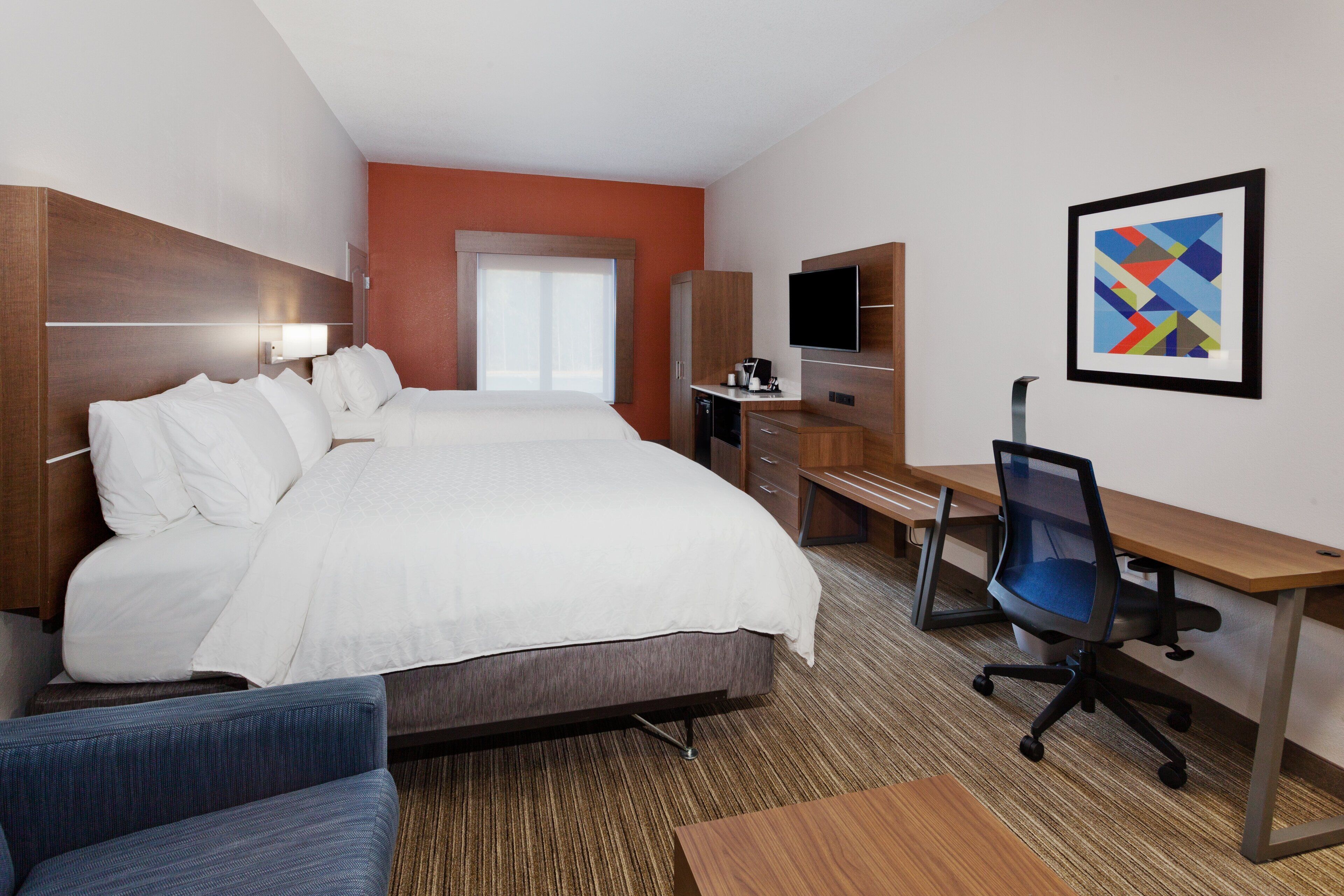 A hotel room with a large bed, a desk, a chair, a television, and a framed picture on the wall.