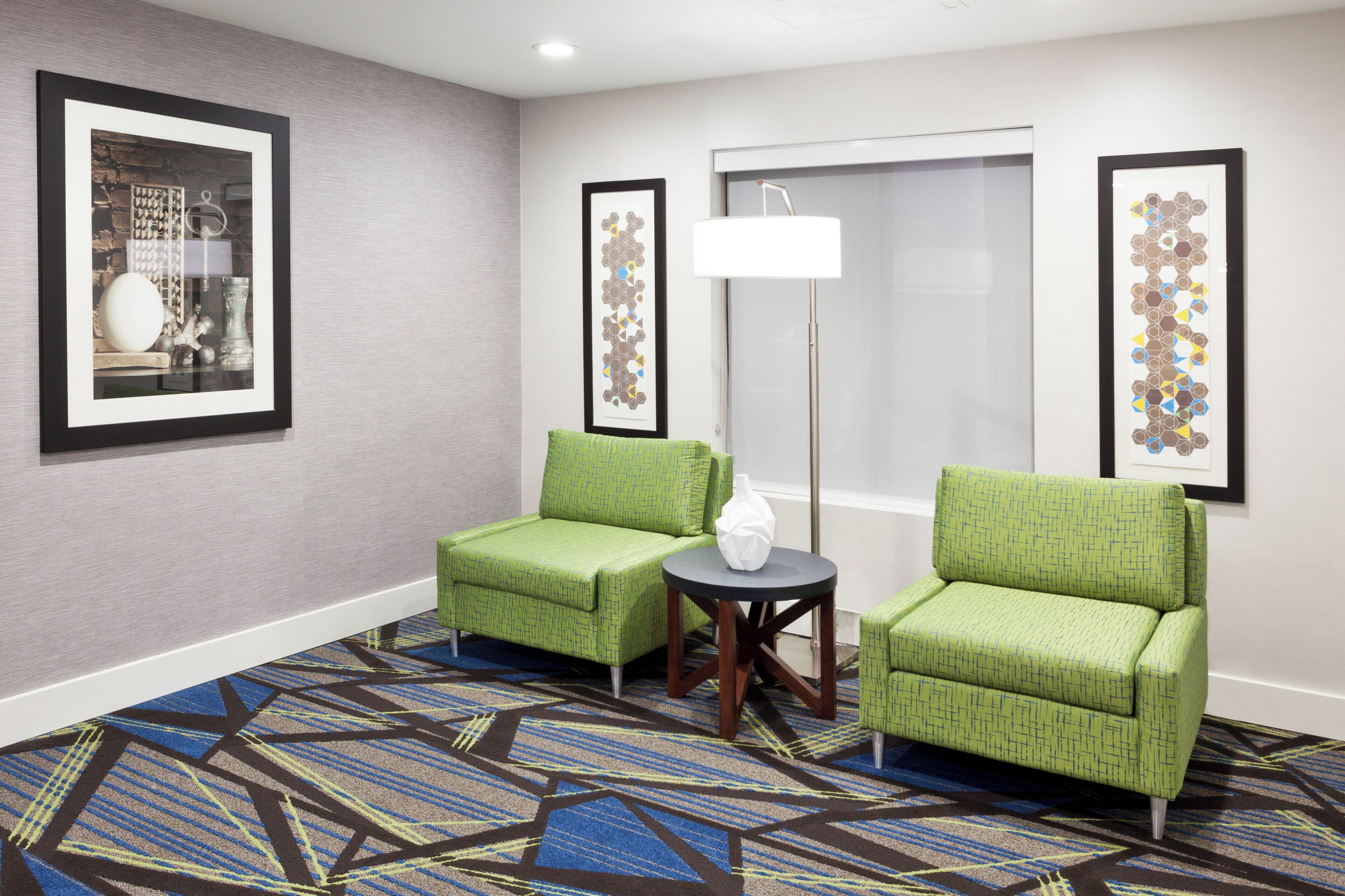Una habitación de hotel con dos sillones verdes, una lámpara de pie y una alfombra estampada.