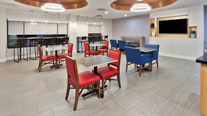 A modern dining area with wooden tables and chairs, a large flat-screen TV, and a kitchen in the background. - Holiday Inn Express & Suites Rome-East by IHG (Rome)