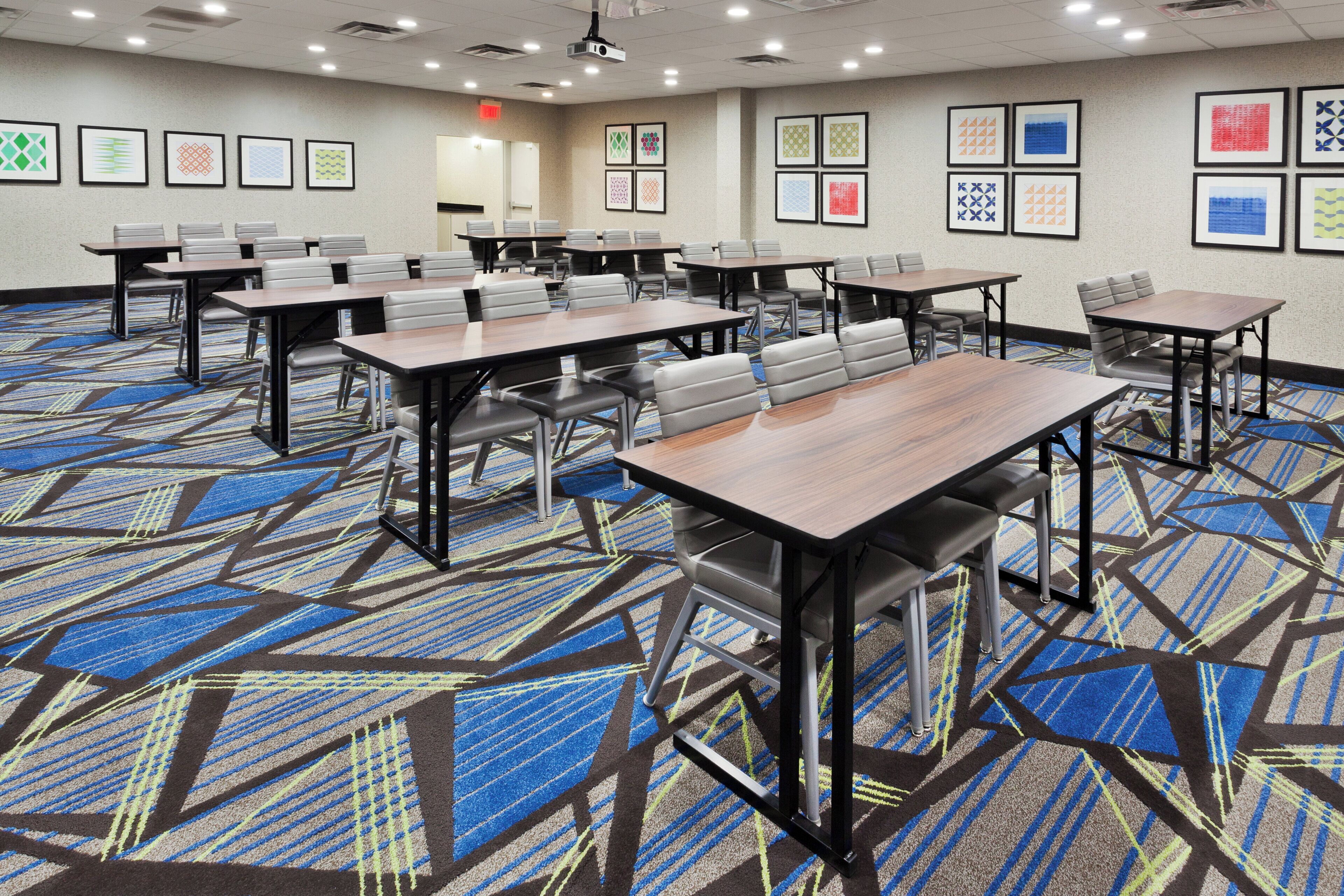 A conference room with multiple tables and chairs, carpeted floor, and framed artwork on the walls.
