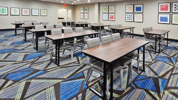 A conference room with multiple tables and chairs, carpeted floor, and framed artwork on the walls.