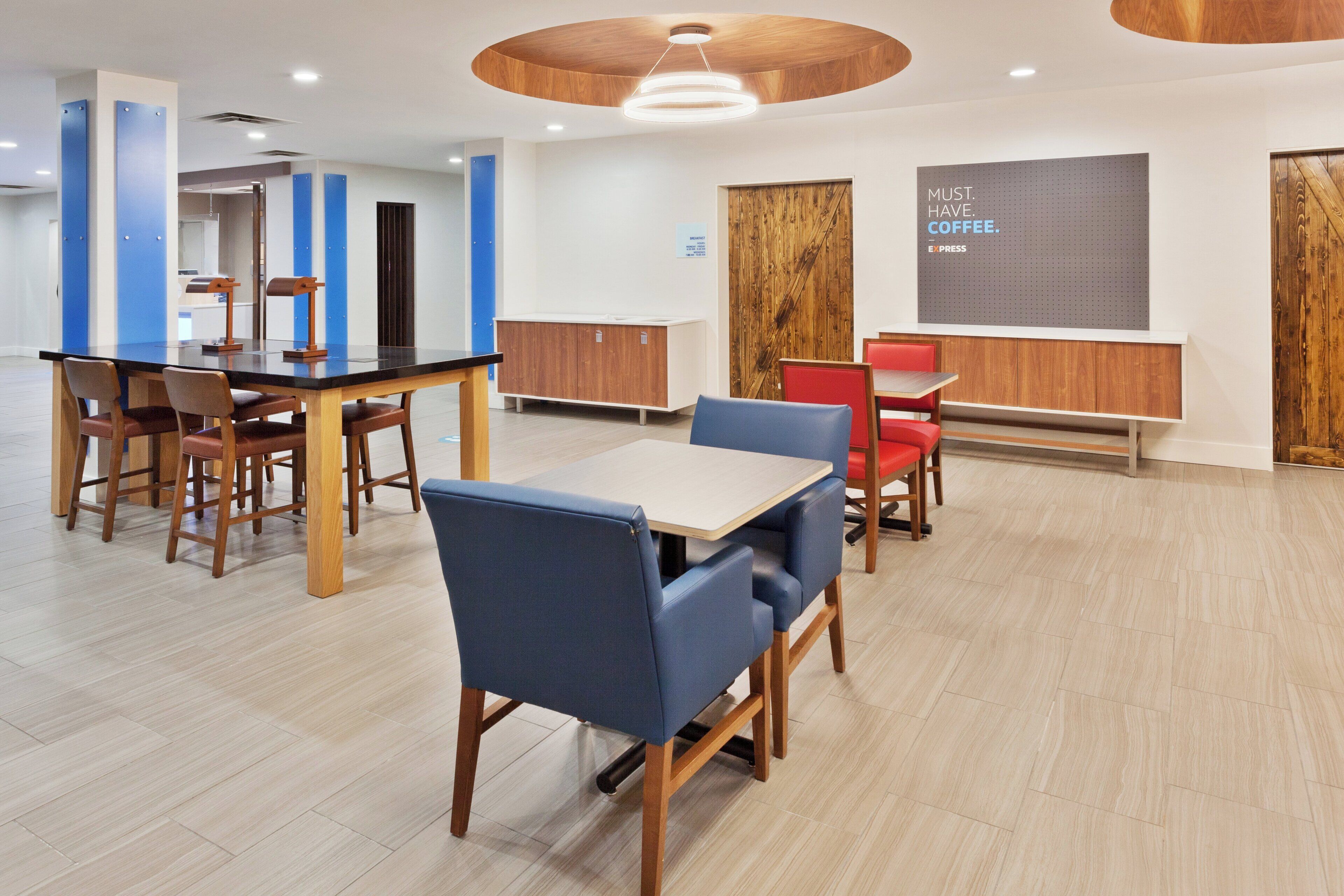 A modern dining area with wooden tables and chairs, a blue accent wall, and a sign indicating a coffee service.