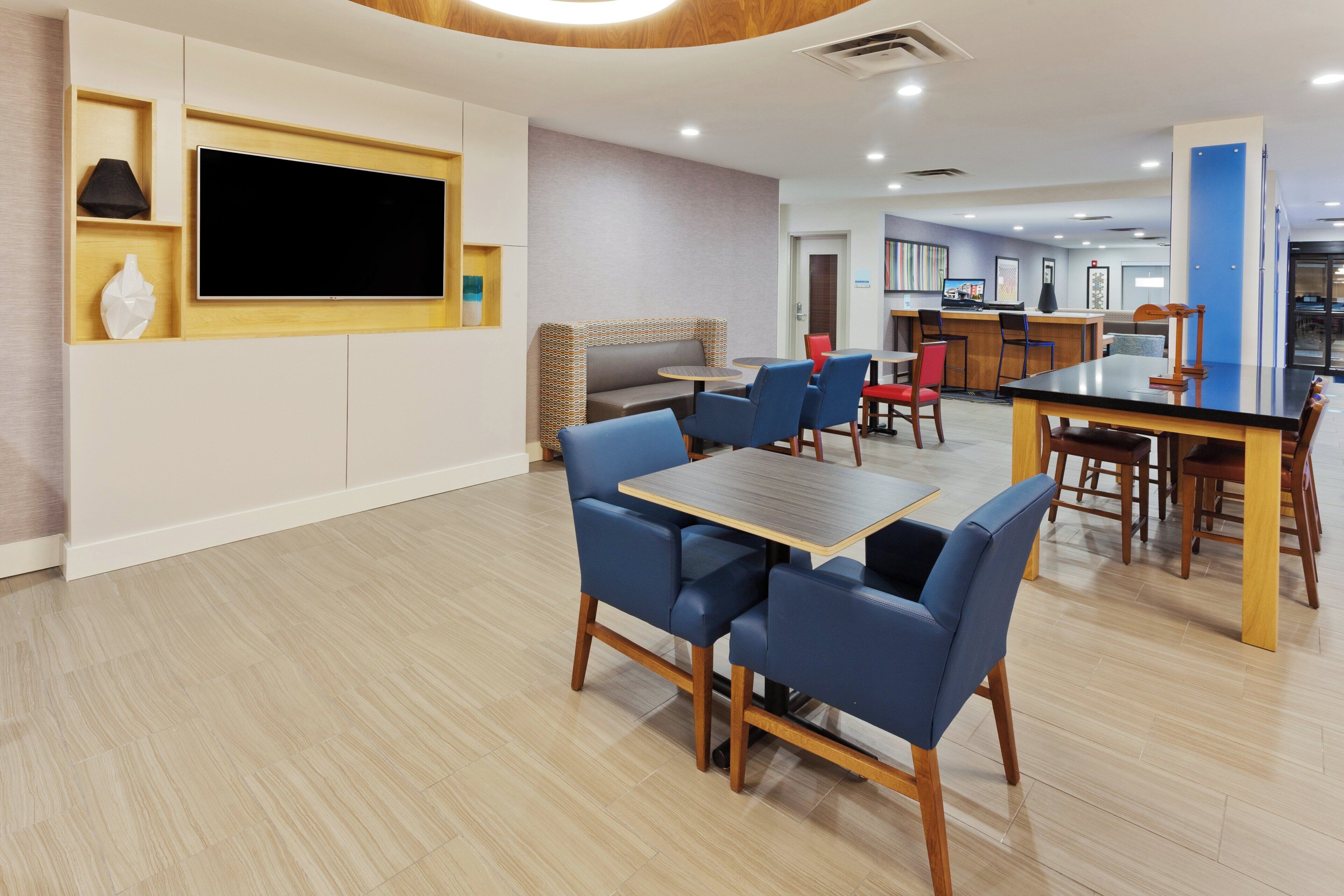 A modern hotel lobby with a seating area, a TV screen, and a reception desk.