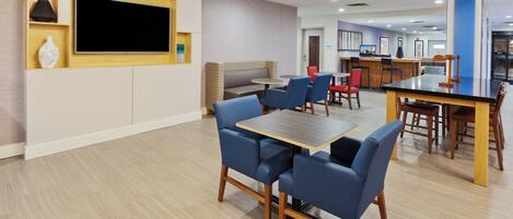 A modern hotel lobby with a seating area, a TV screen, and a reception desk.
