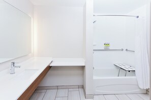 Un baño moderno con lavamanos, espejo y zona de ducha blancos.