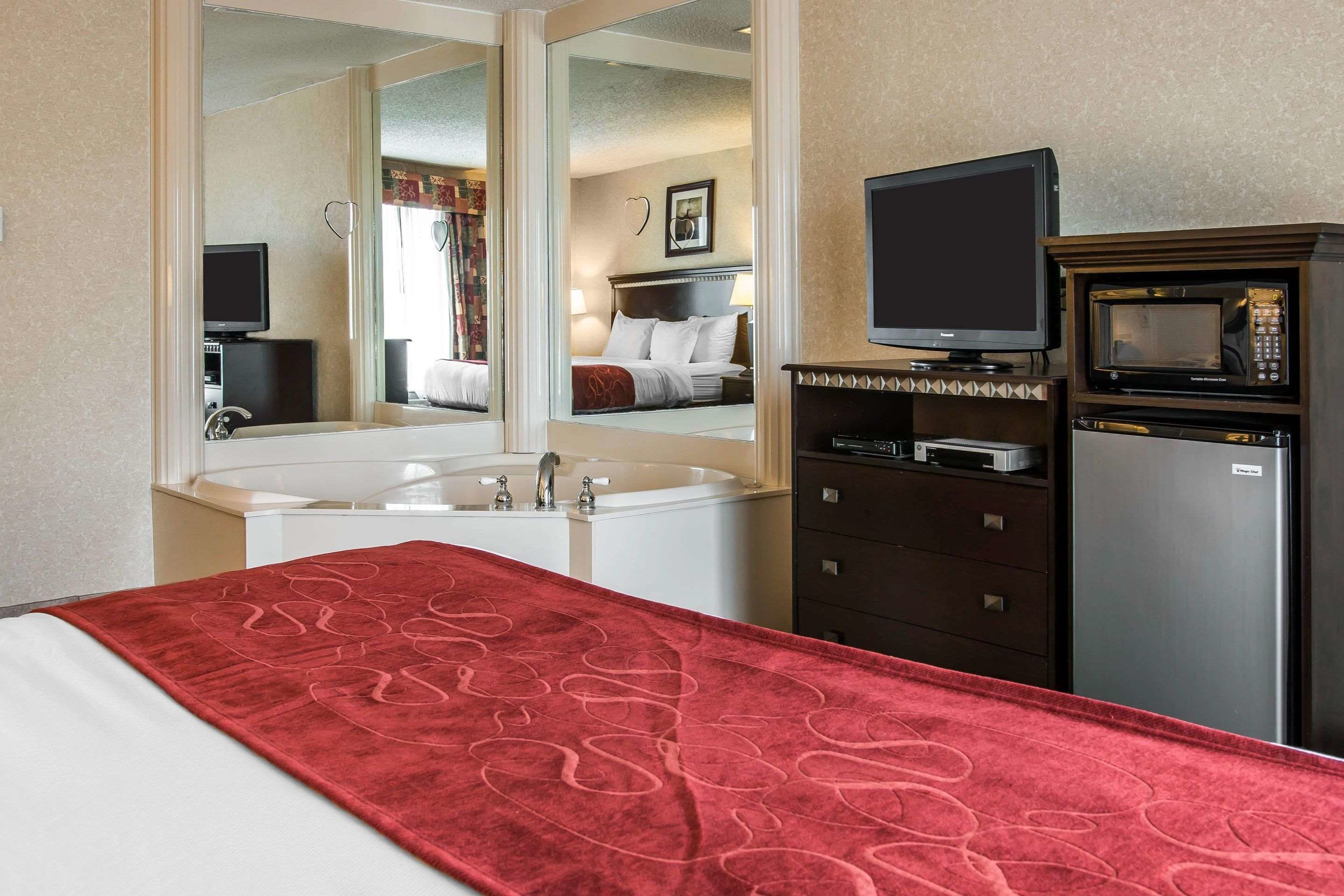 A hotel room with a bed, a red towel, a large mirror, a television, a microwave, and a refrigerator.