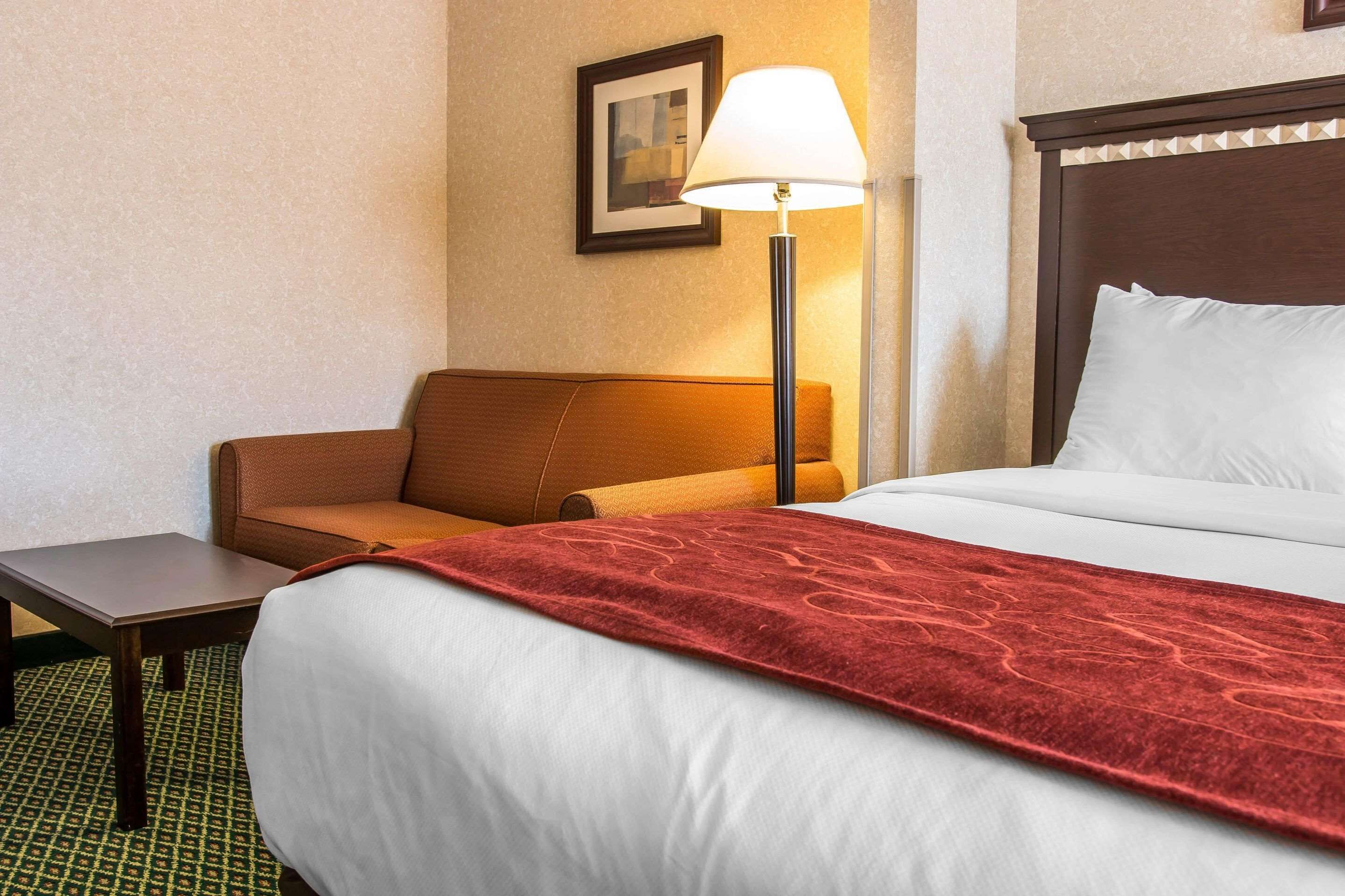A hotel room with a bed, a desk, a chair, a lamp, and a framed picture on the wall.