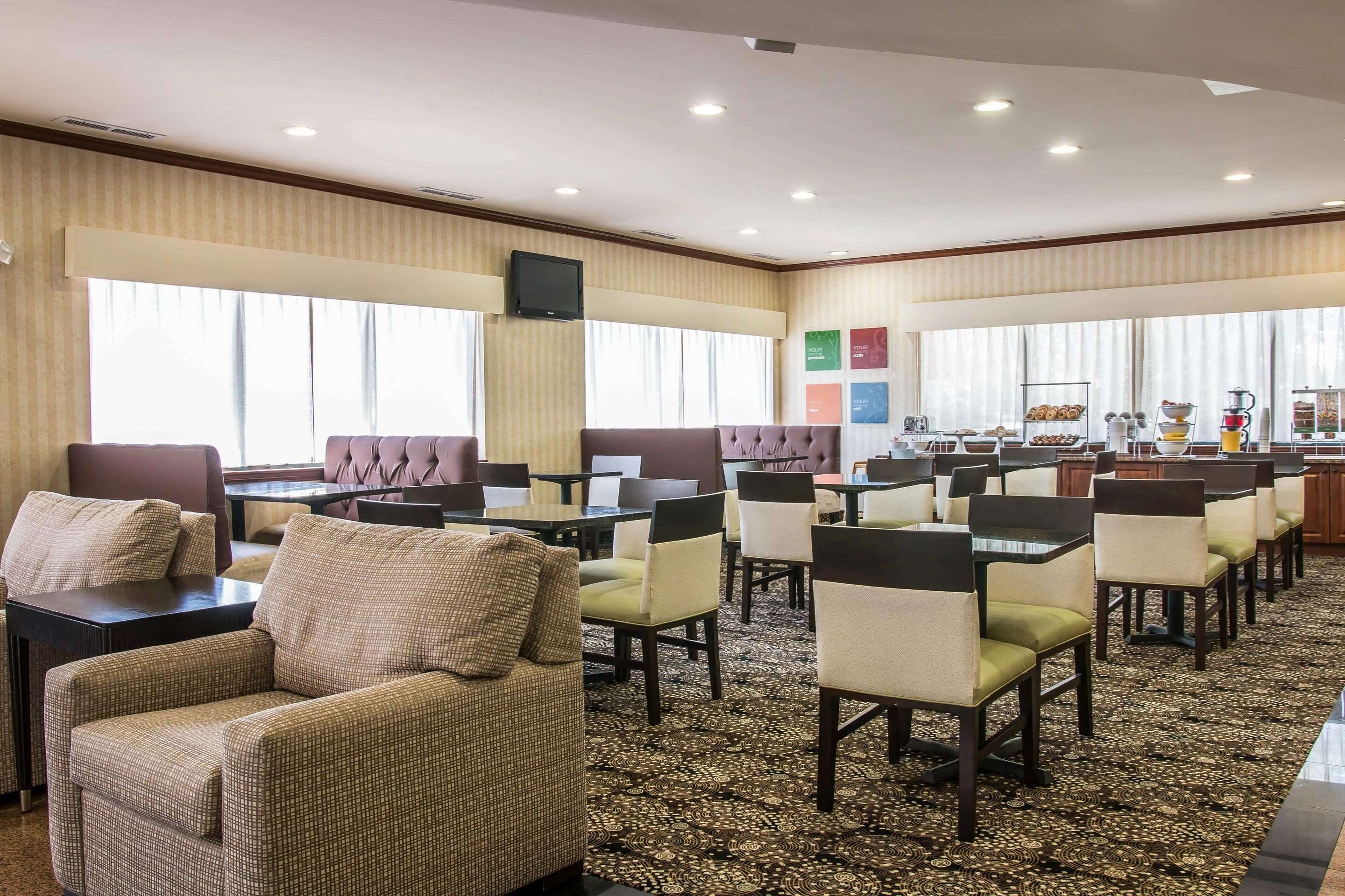 A hotel dining area with multiple tables and chairs, a television mounted on the wall, and a buffet setup.