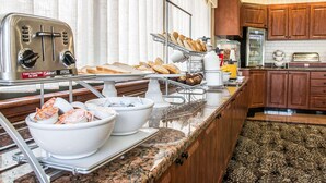 A hotel kitchen with a toaster, bread, pastries, and a refrigerator. - Comfort Suites Canton - Detroit (Canton)