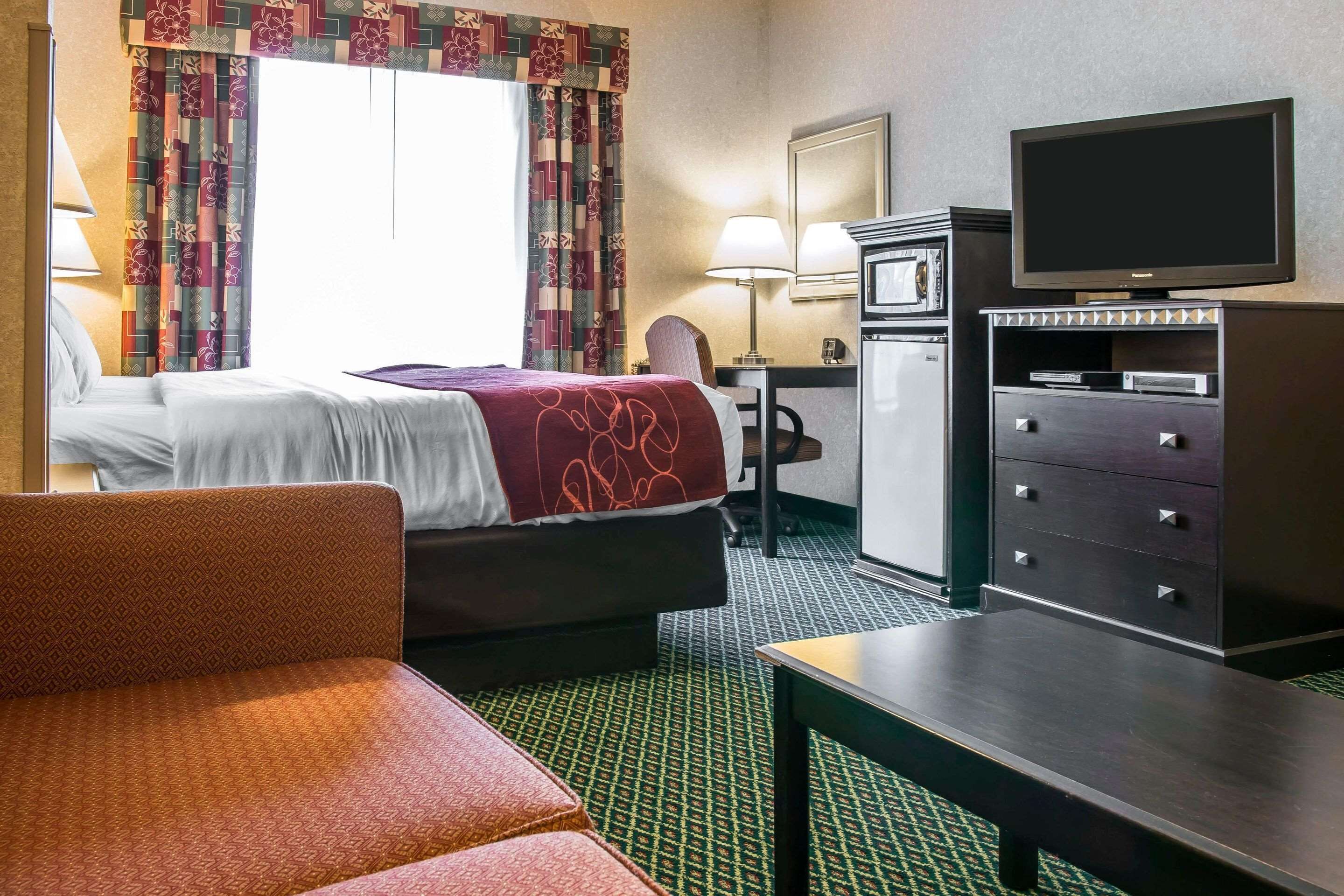 Quarto de hotel com cama, escrivaninha, televisão e cómoda.