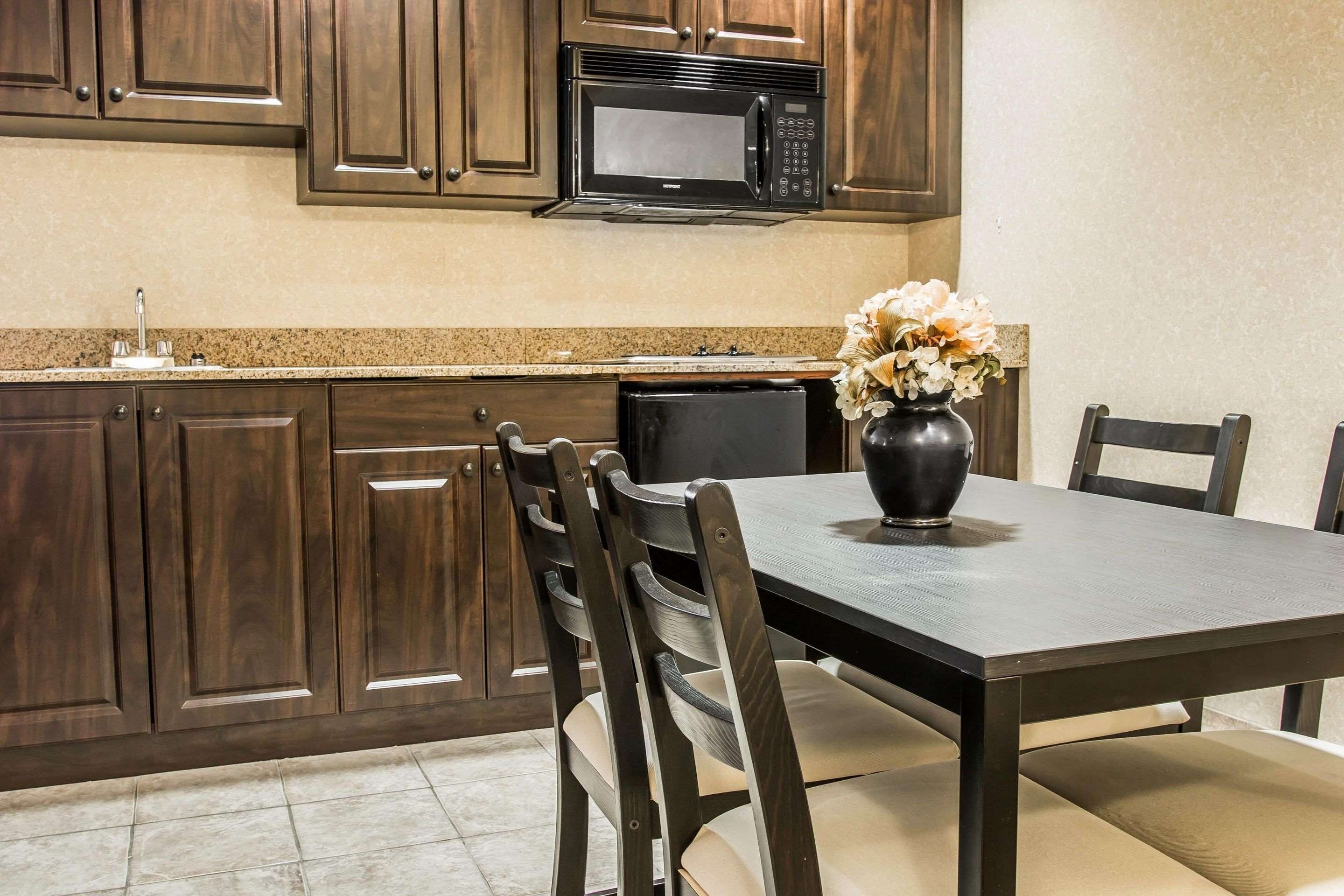 A kitchen with dark wood cabinets, a black microwave, a dining table with chairs, and a vase with flowers.