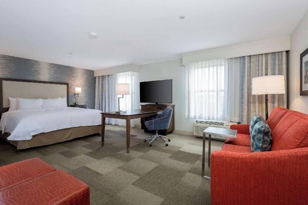 A hotel room with a bed, a desk, a TV, a red sofa, and a small table.