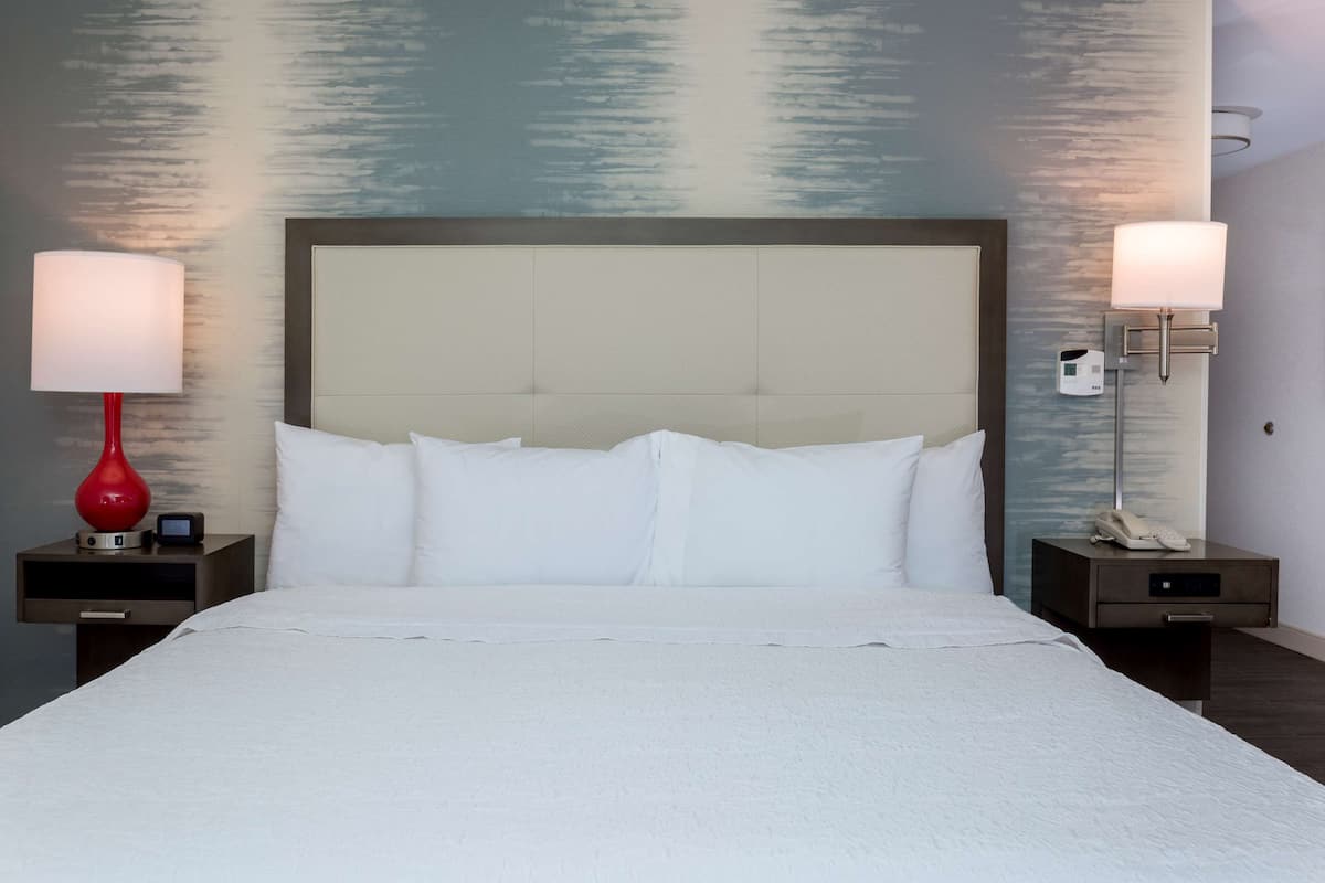 A hotel room with a large bed, two bedside tables, a red lamp, and a wall-mounted phone.