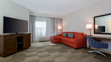 Habitación de hotel con televisión de pantalla plana, un sofá, un escritorio con una silla y un espejo grande.