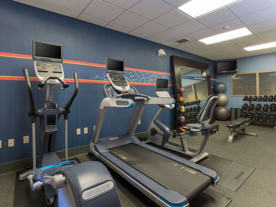 A gym with treadmills, elliptical machines, and a wall-mounted TV.