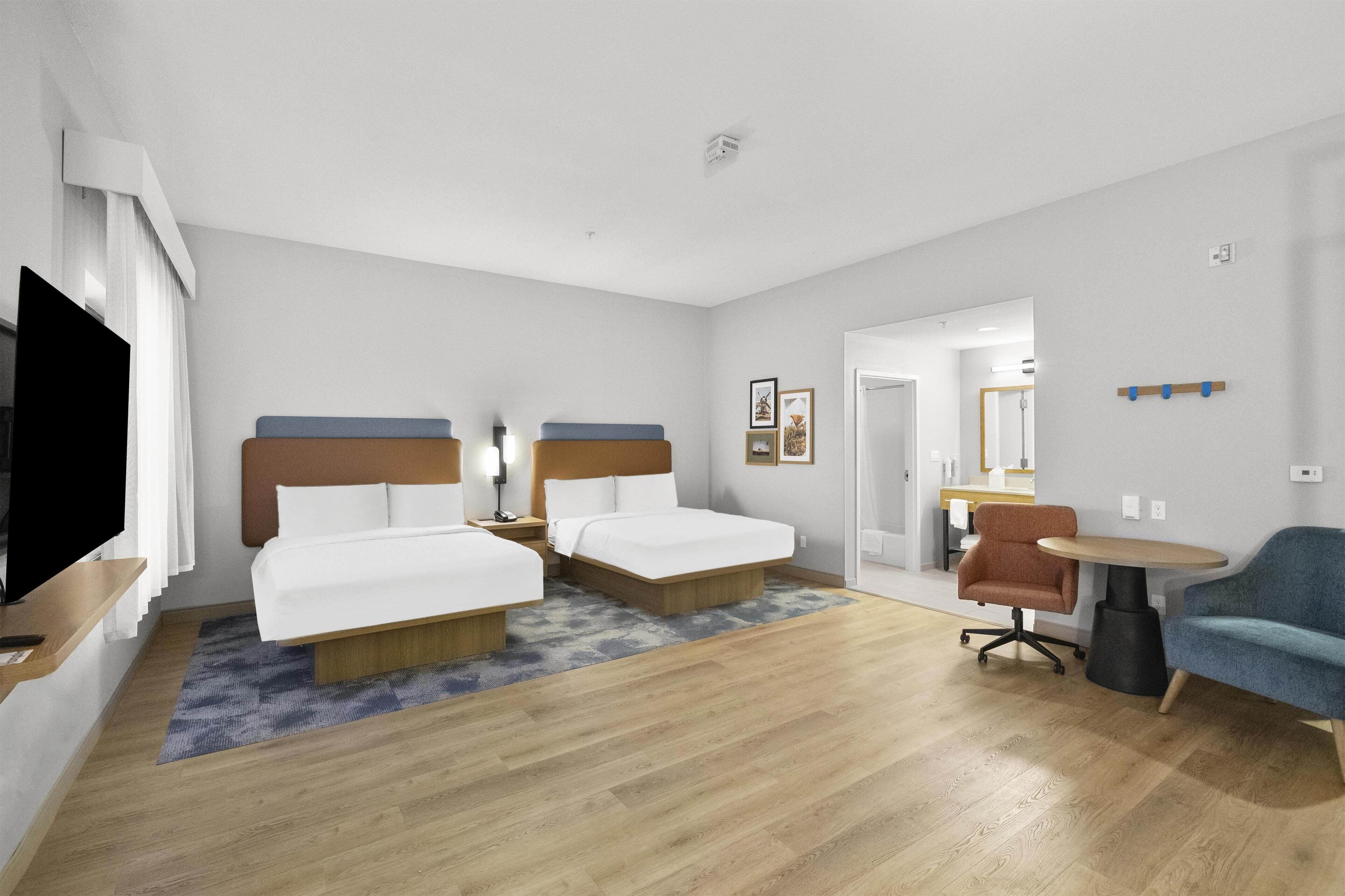 A hotel room with two beds, a TV, a desk, and a chair.