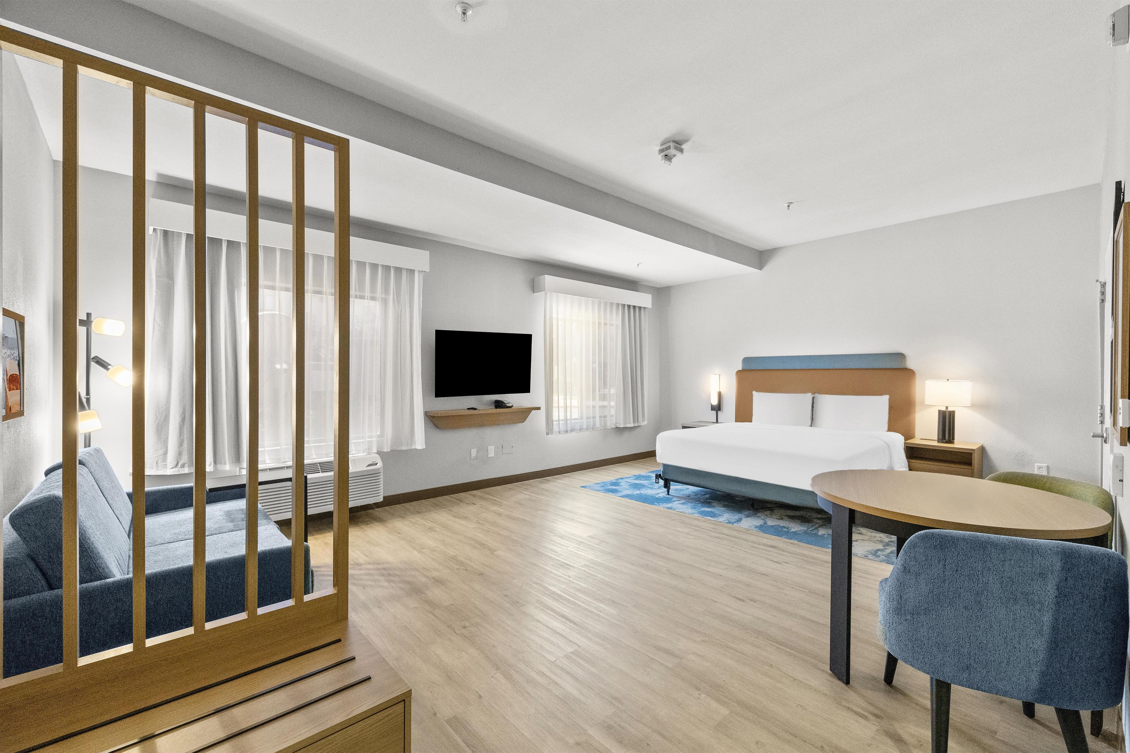 A hotel room with a bed, a desk, a chair, a TV, and a window with curtains.