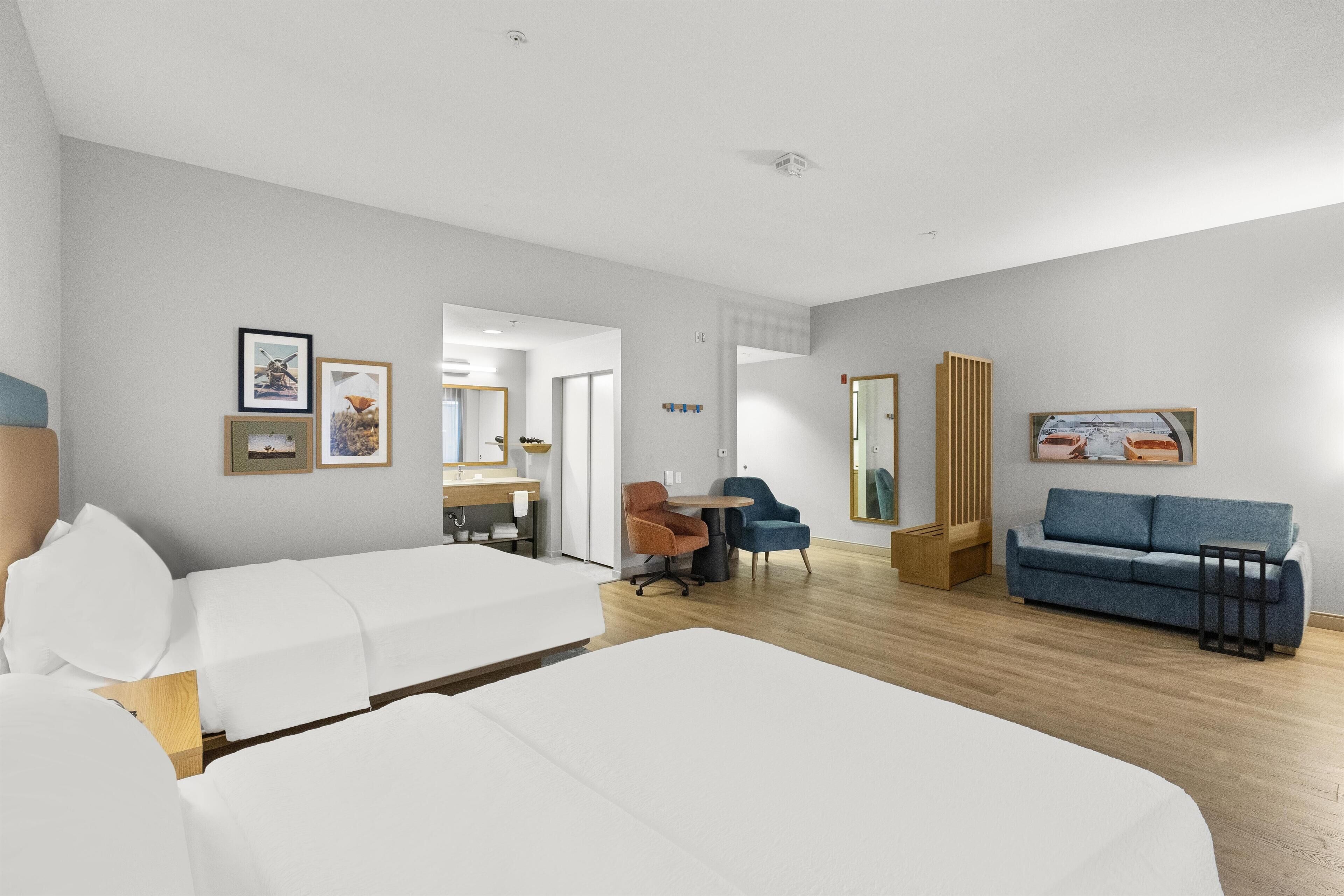 A hotel room with a bed, a desk, a chair, a sofa, and a mirror.
