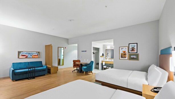 Una habitación de hotel moderna con una cama grande, un sofá azul, una mesita de madera y un escritorio con sillas.