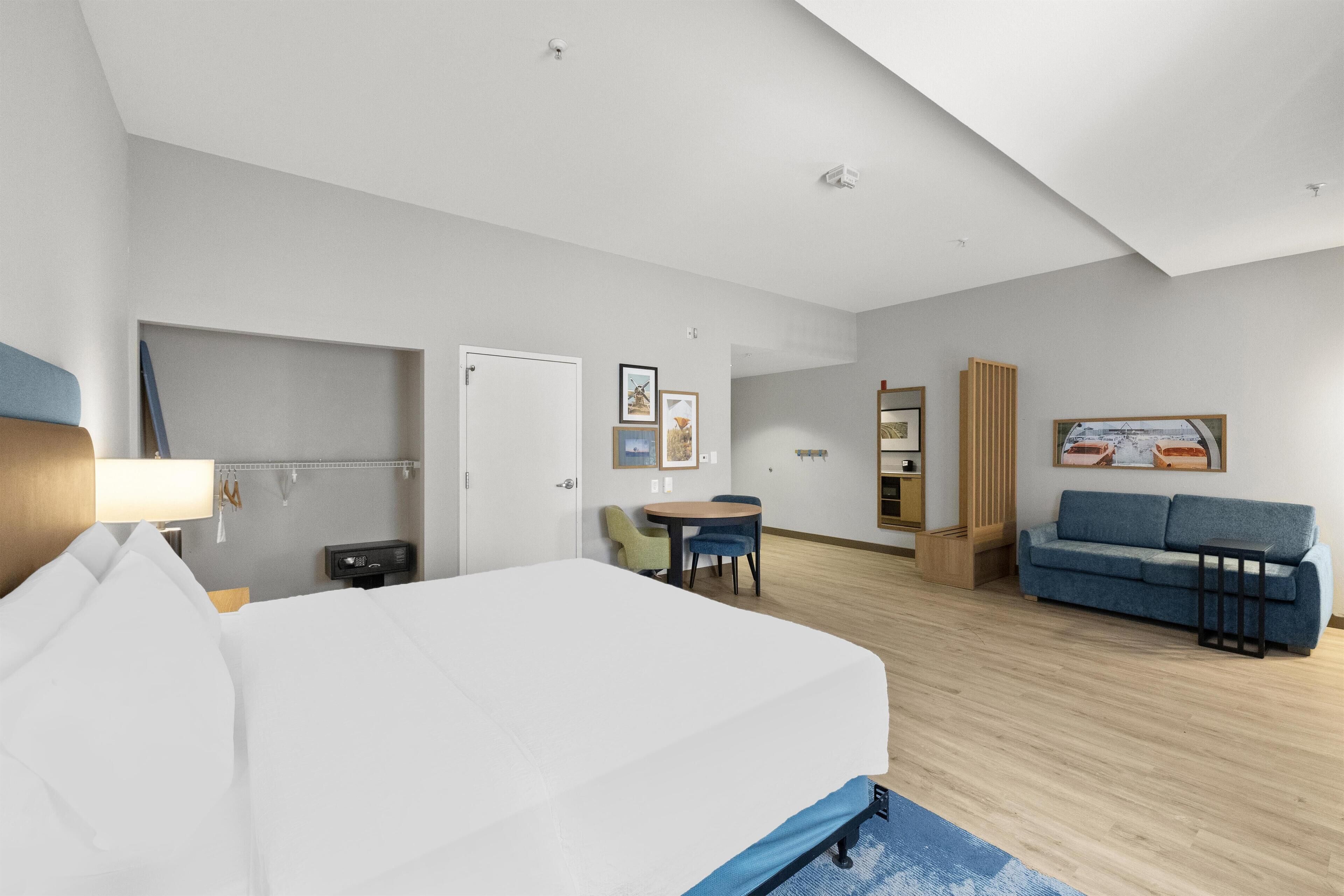 A hotel room with a bed, a desk, a chair, a sofa, and a small table.