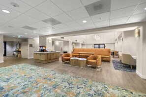 A spacious hotel lobby with a central seating area, a kitchenette, and a patterned carpet.