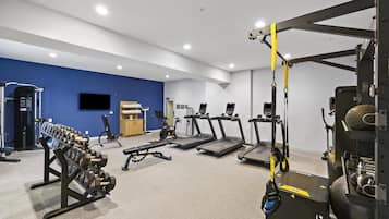 Een sportschool met loopbanden, krachttoestellen en een squat rek.