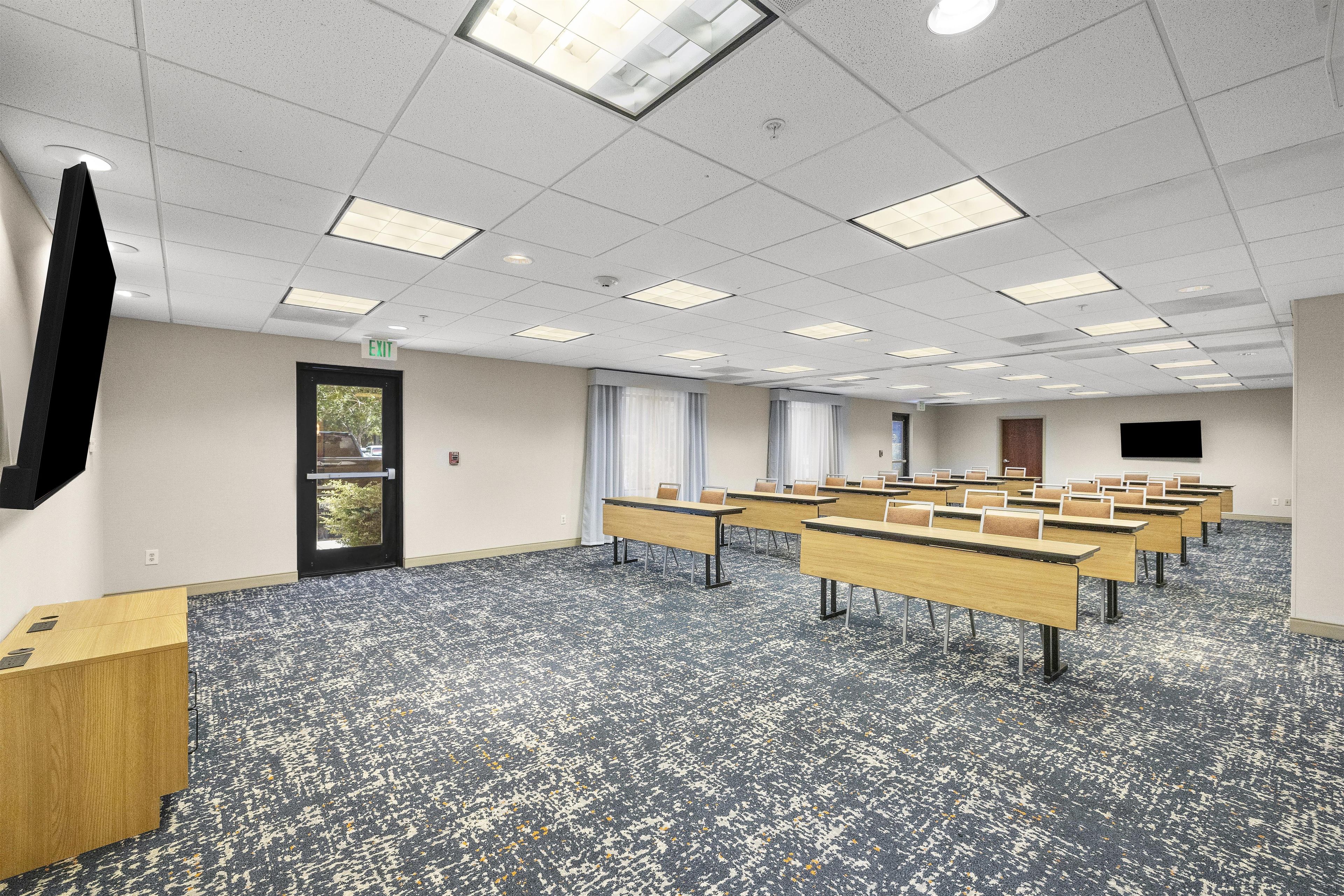 Une salle de conférence équipée de plusieurs tables et chaises, d’un téléviseur à écran plat fixé au mur et d’une porte avec un panneau indiquant la sortie.