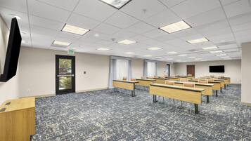 Une salle de conférence équipée de plusieurs tables et chaises, d’un téléviseur à écran plat fixé au mur et d’une porte avec un panneau indiquant la sortie.