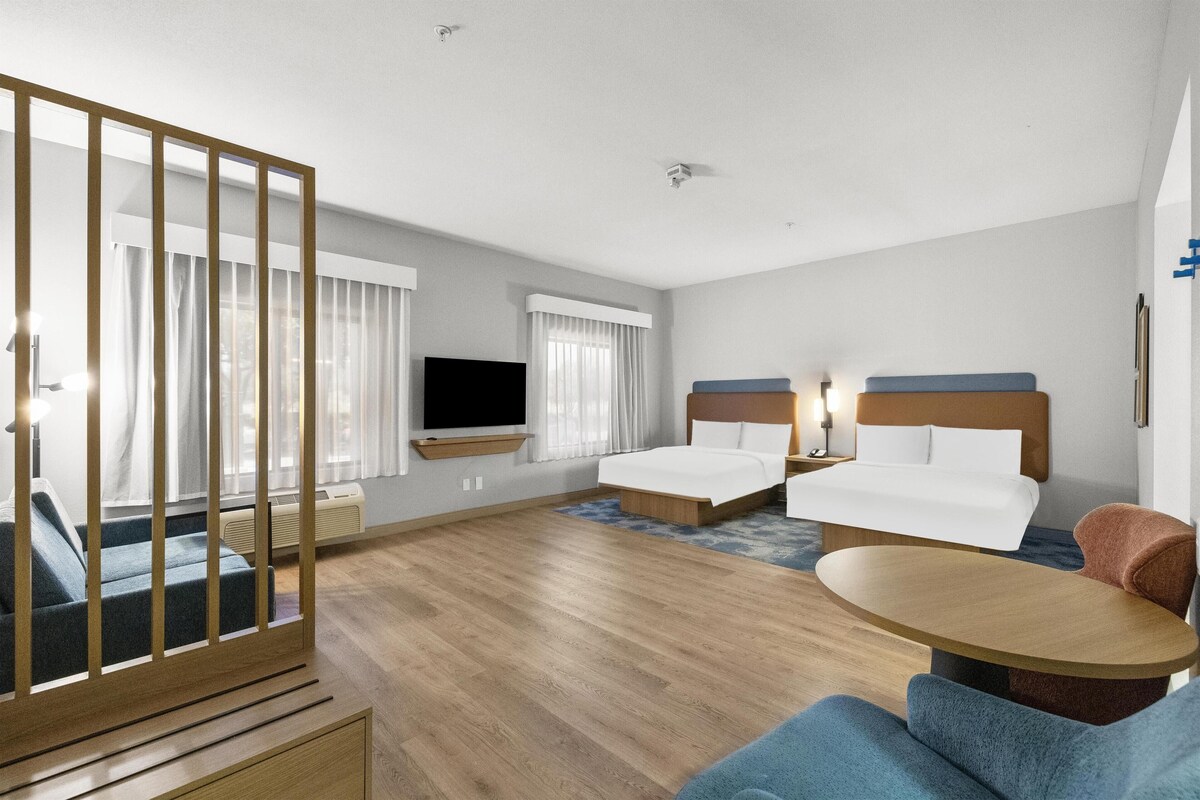 A hotel room with a large bed, a smaller bed, a TV, a desk, and a seating area.