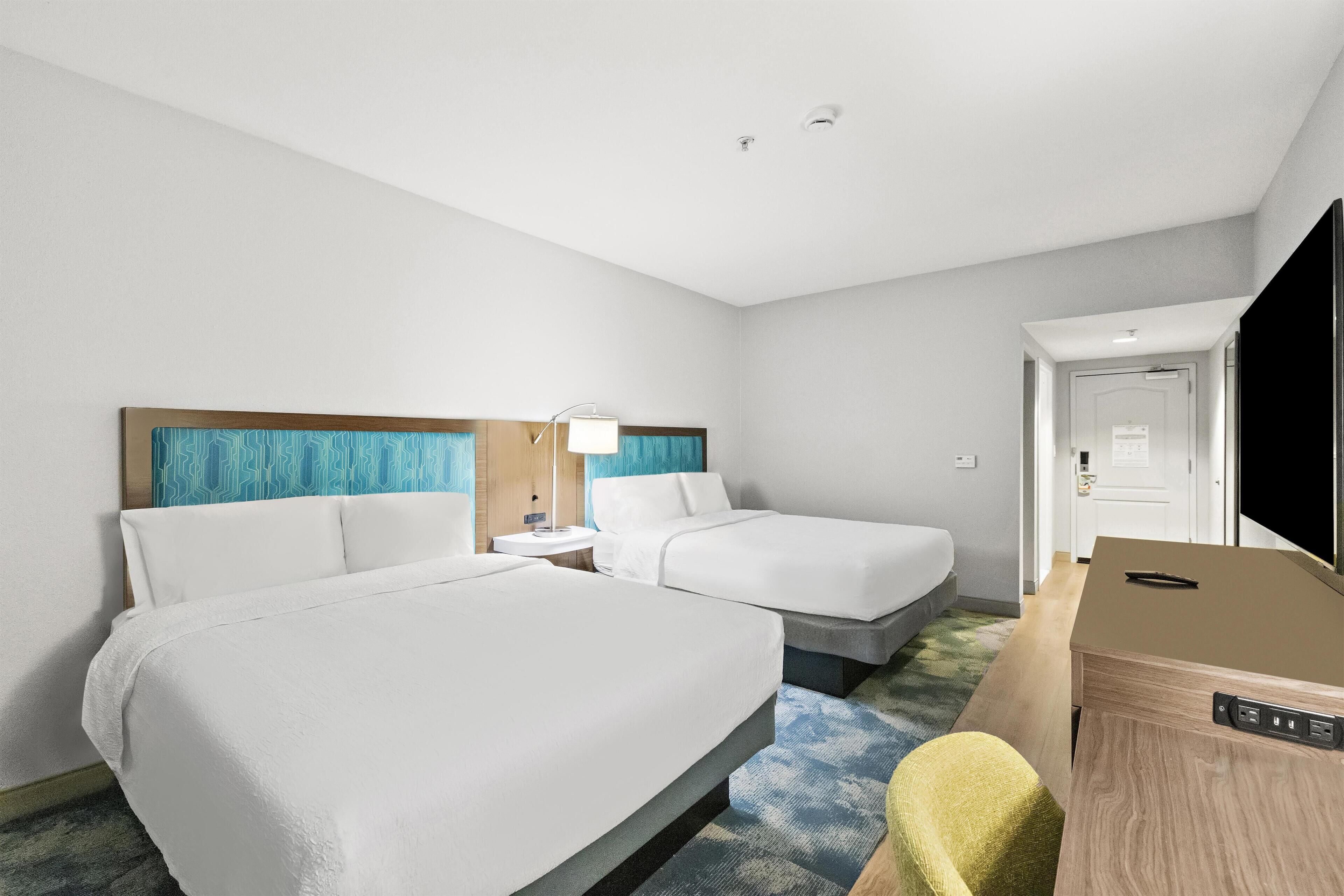 Habitación de hotel con dos camas, un escritorio, una silla y un televisor.