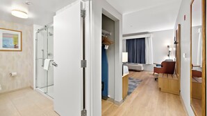 Una habitación de hotel moderna con ducha de vidrio, un escritorio de madera, una silla y una cama.