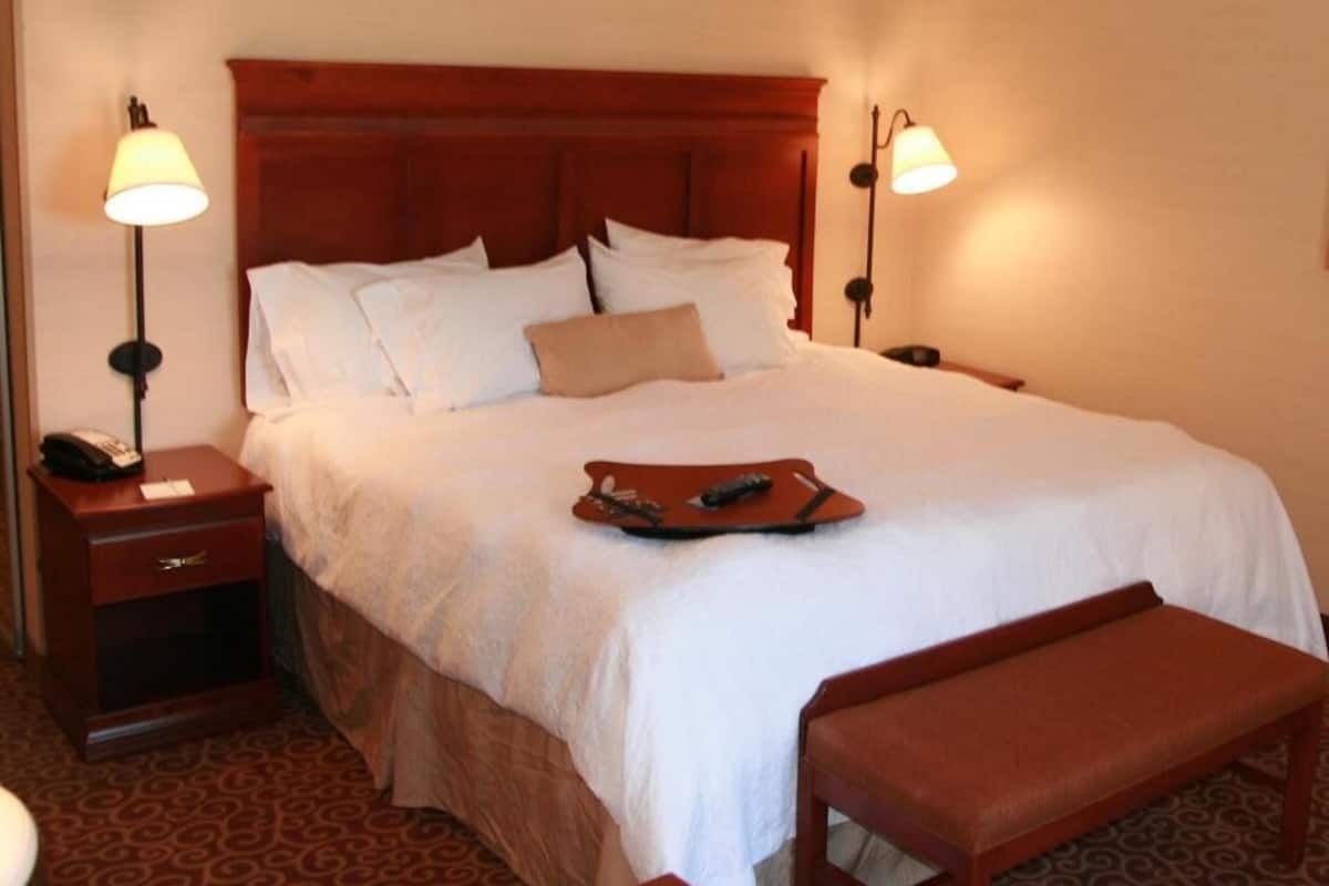 A hotel room with a large bed, two bedside tables, a bedside lamp, a bedside phone, a tray table, and a bench.